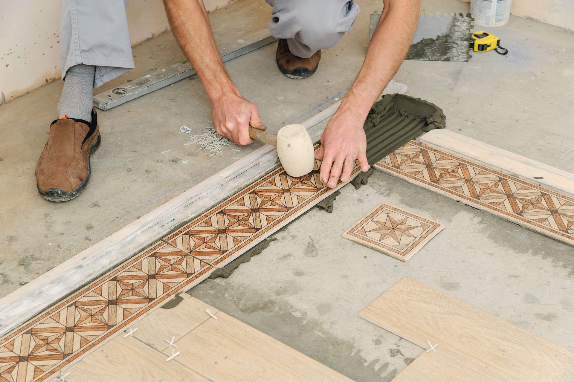 A man is laying tiles on the floor with a rubber mallet.