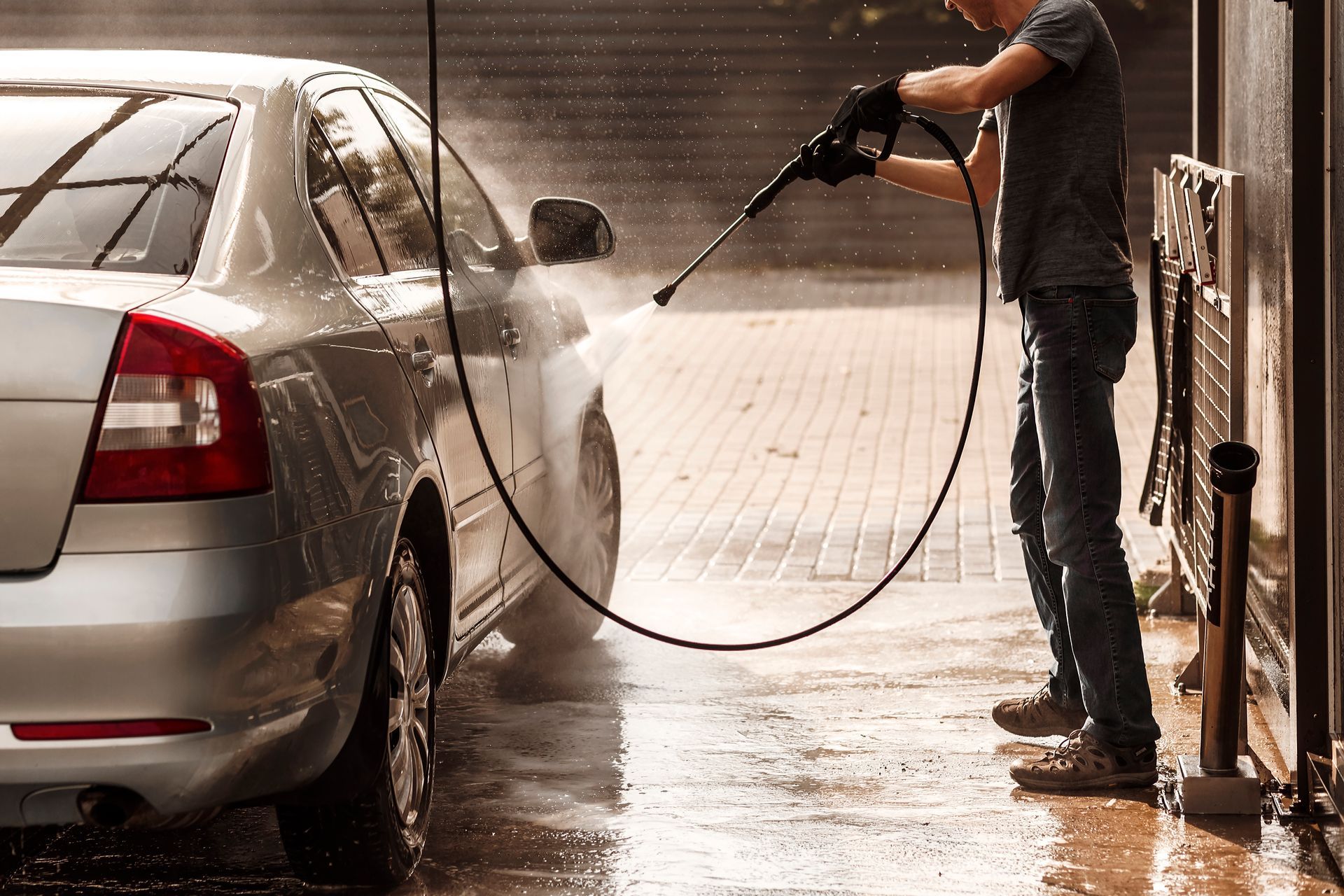 A man is washing a car with a high pressure washer.