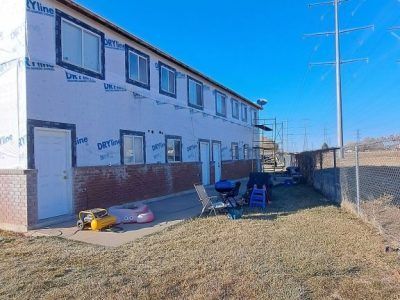 Two-story building with unfinished siding, brick base, and yard.