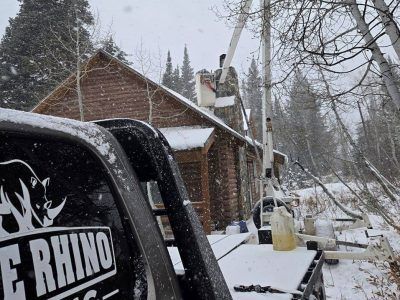 Truck with boom lift at a snow-covered cabin in a forest; worker on the roof.