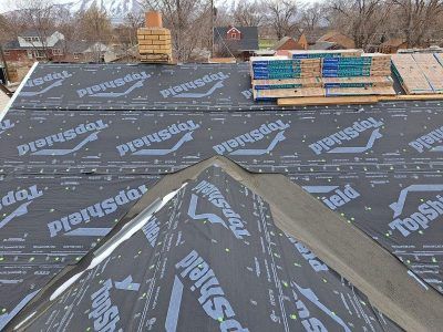 Roof partially covered in black underlayment; shingles and materials stacked nearby.