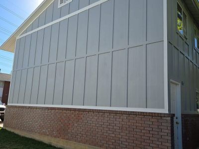 Gray siding with vertical grooves over a brick foundation on a house.