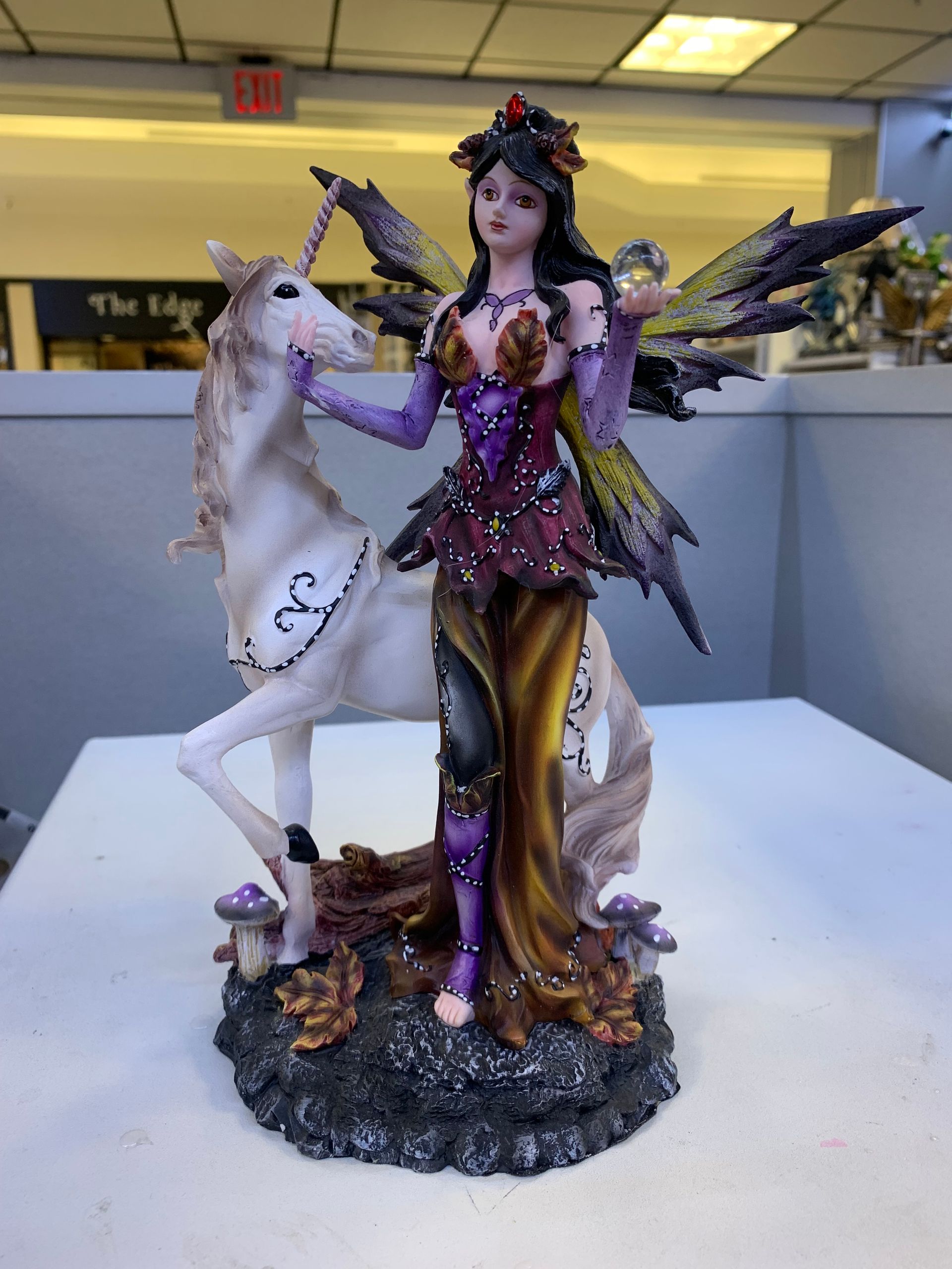 A statue of a fairy standing next to a unicorn on a table.