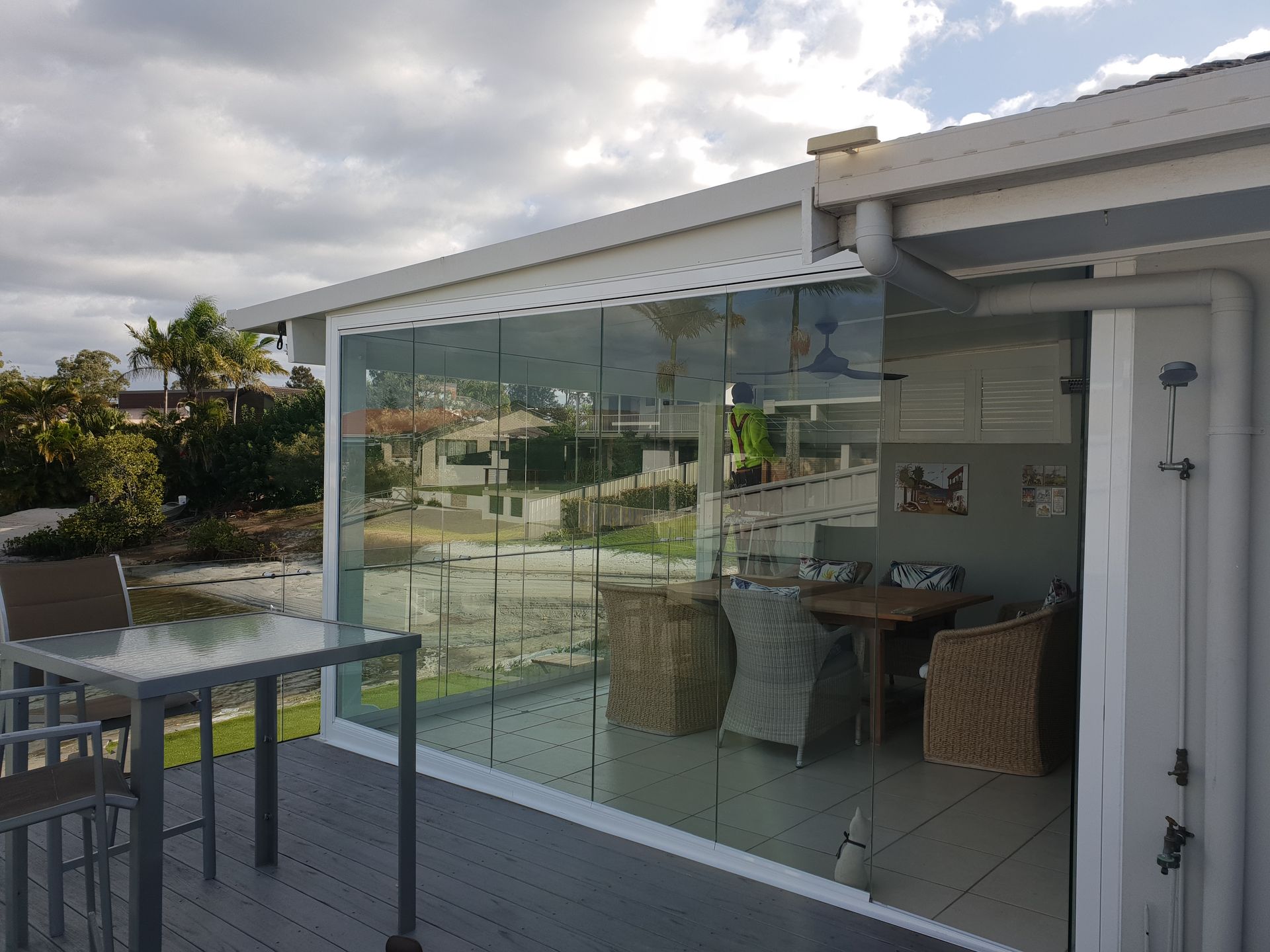 Patio with glass sliding doors, outdoor table and chairs, and a cloudy sky reflected in the glass