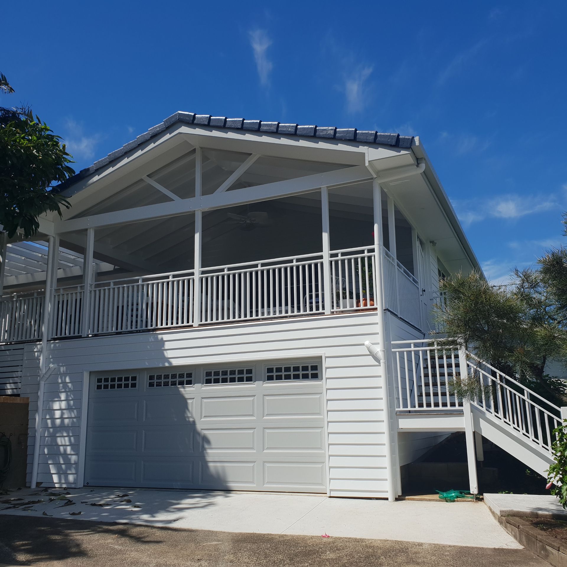 White two-story house with garage, wraparound porch, and exterior stairs under a blue sky