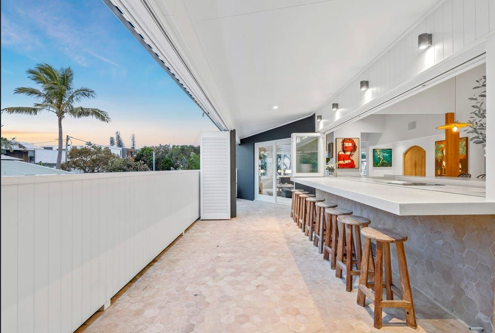 Modern outdoor bar with white awning, wooden stools, and sunset view beyond a patio fence