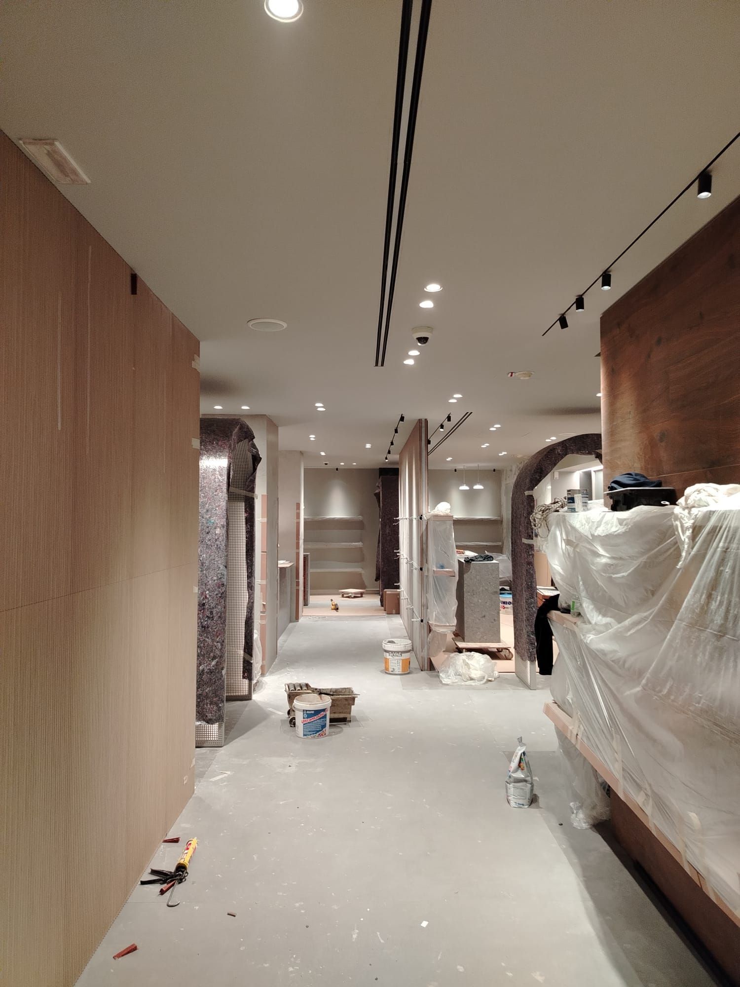 Interno di un negozio in costruzione con pannelli in legno chiaro, illuminazione da incasso e pavimento in cemento.