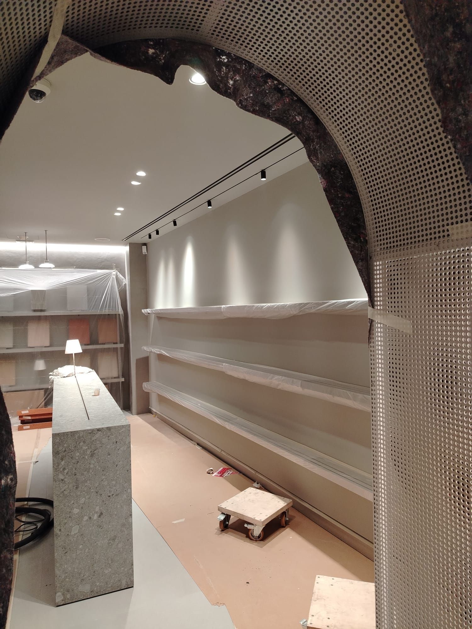 Interno di uno spazio commerciale in costruzione, con scaffali e infissi in cemento; colori neutri.