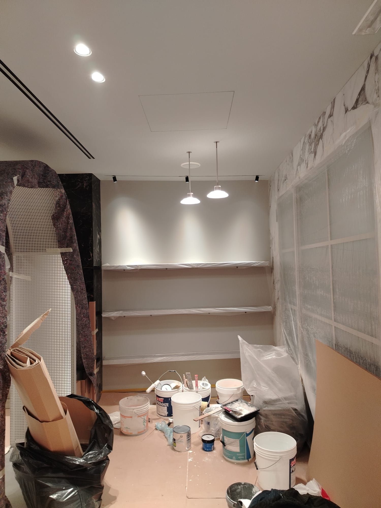 Interno di un negozio in costruzione con scaffali, secchi di vernice e teli di plastica.
