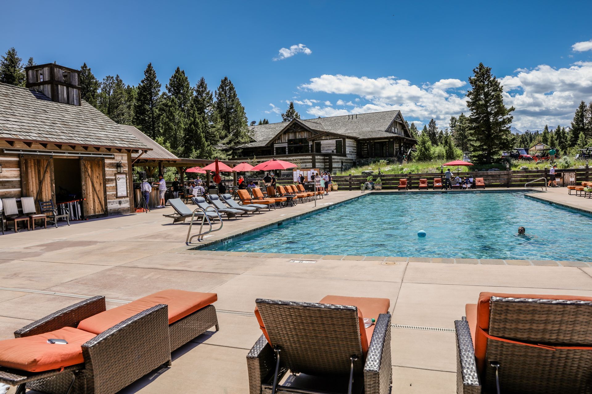 A large swimming pool surrounded by chairs and umbrellas with a house in the background.
