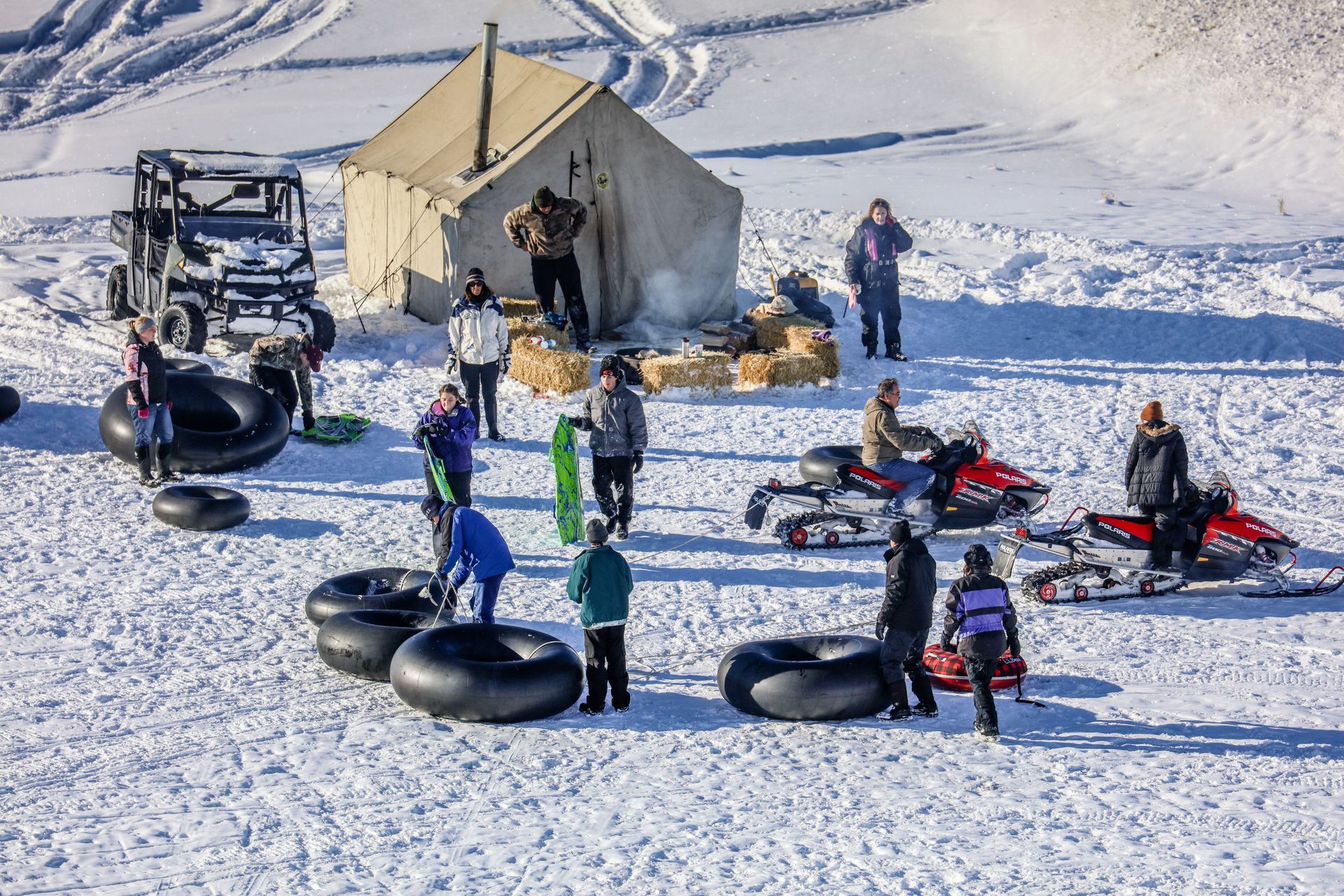 A group of people are riding snowmobiles and tubing in the snow.
