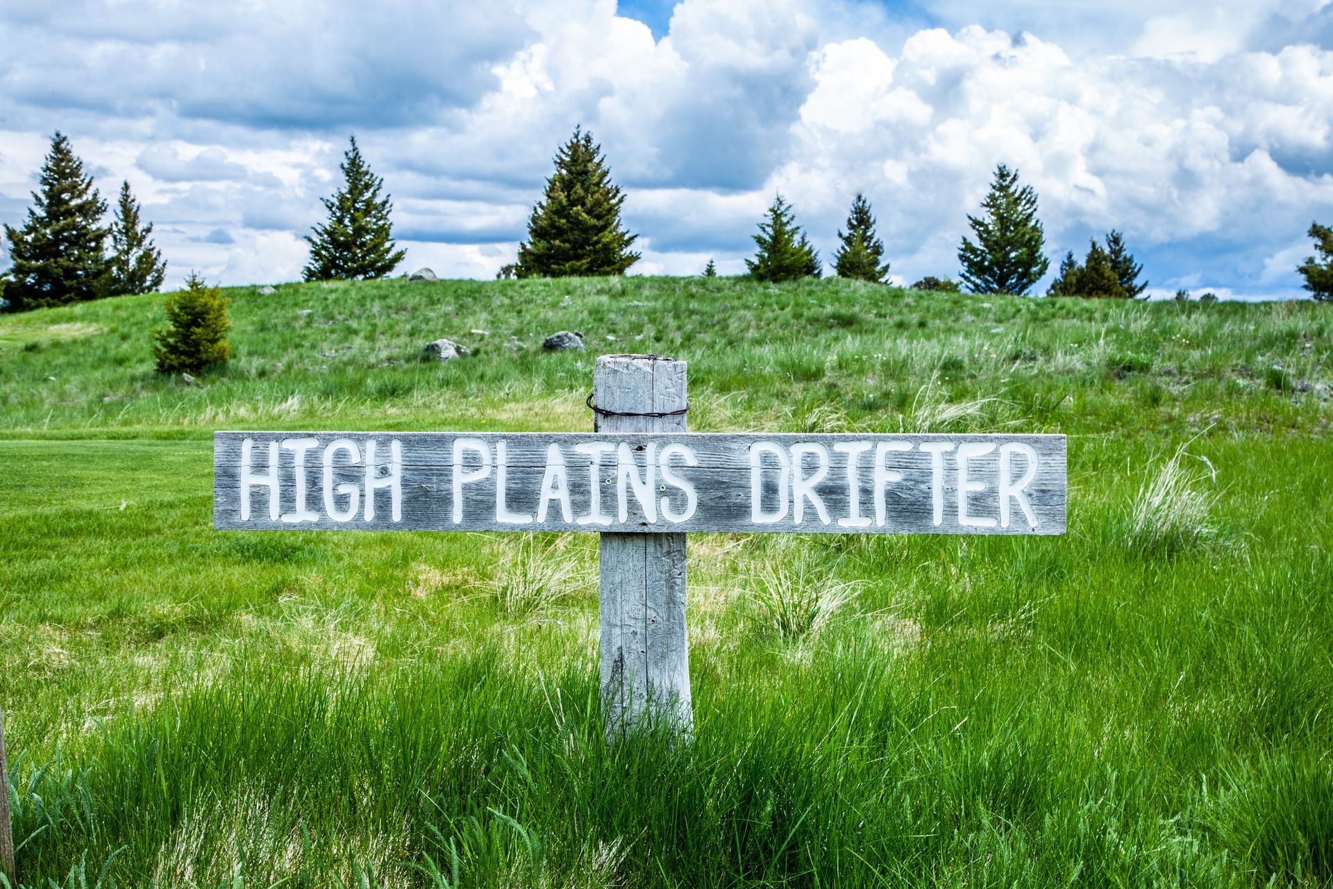 A sign that says high plains drifter is in the middle of a grassy field.