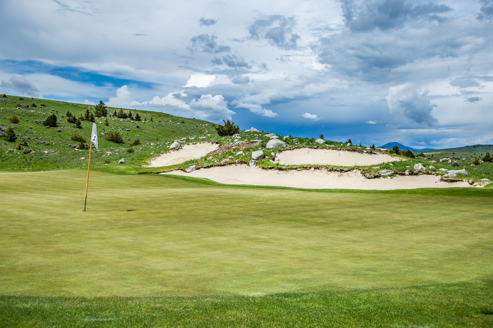 A golf course with a green and sand dunes on a cloudy day.
