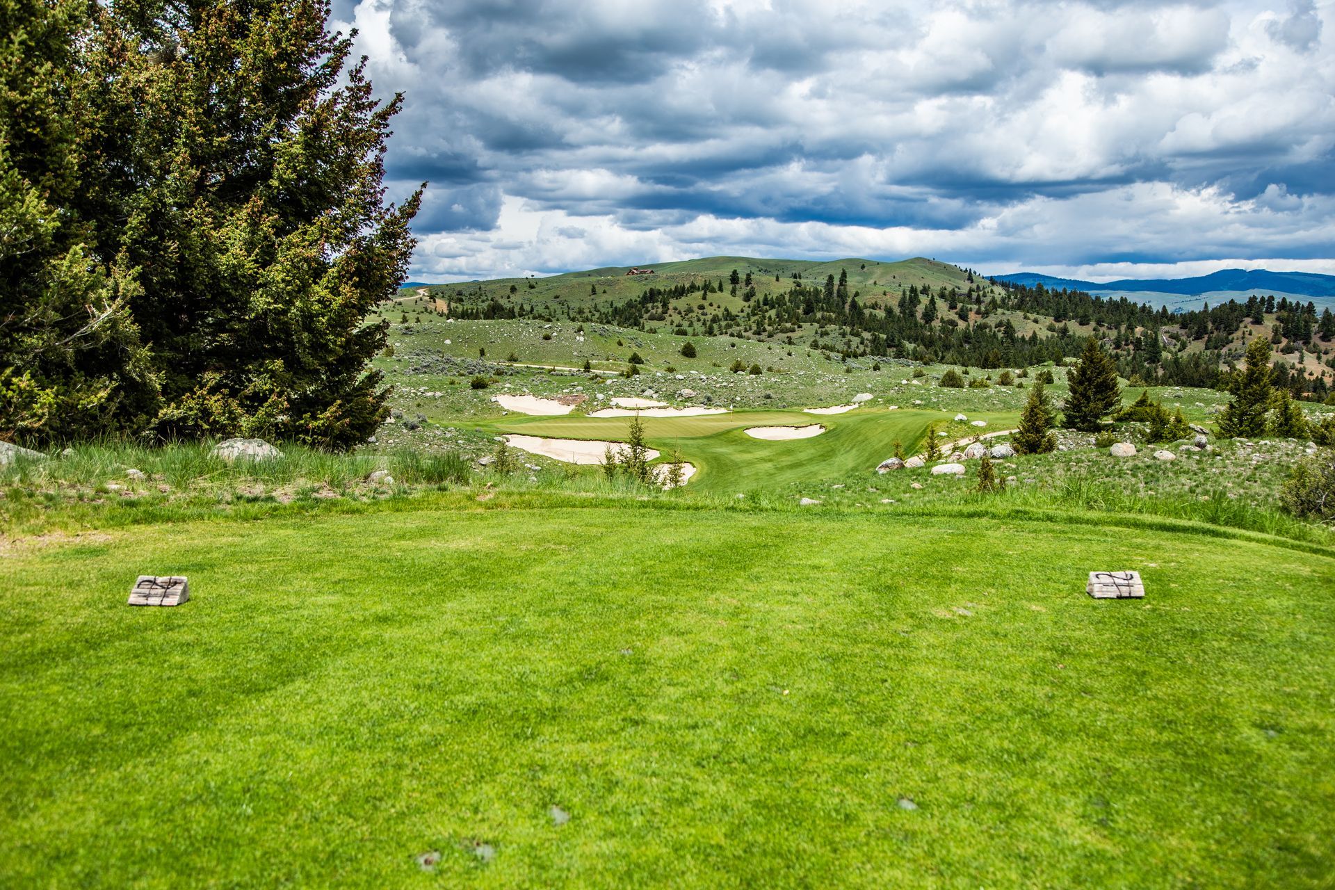 A golf course in the middle of a grassy field with mountains in the background.