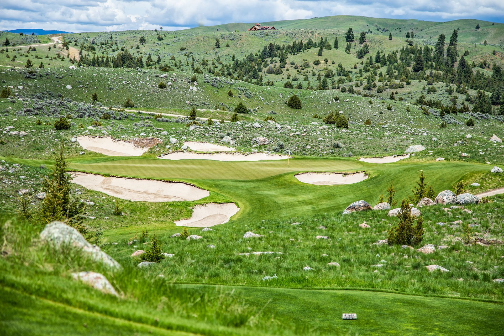 A golf course in the middle of a grassy field with mountains in the background.