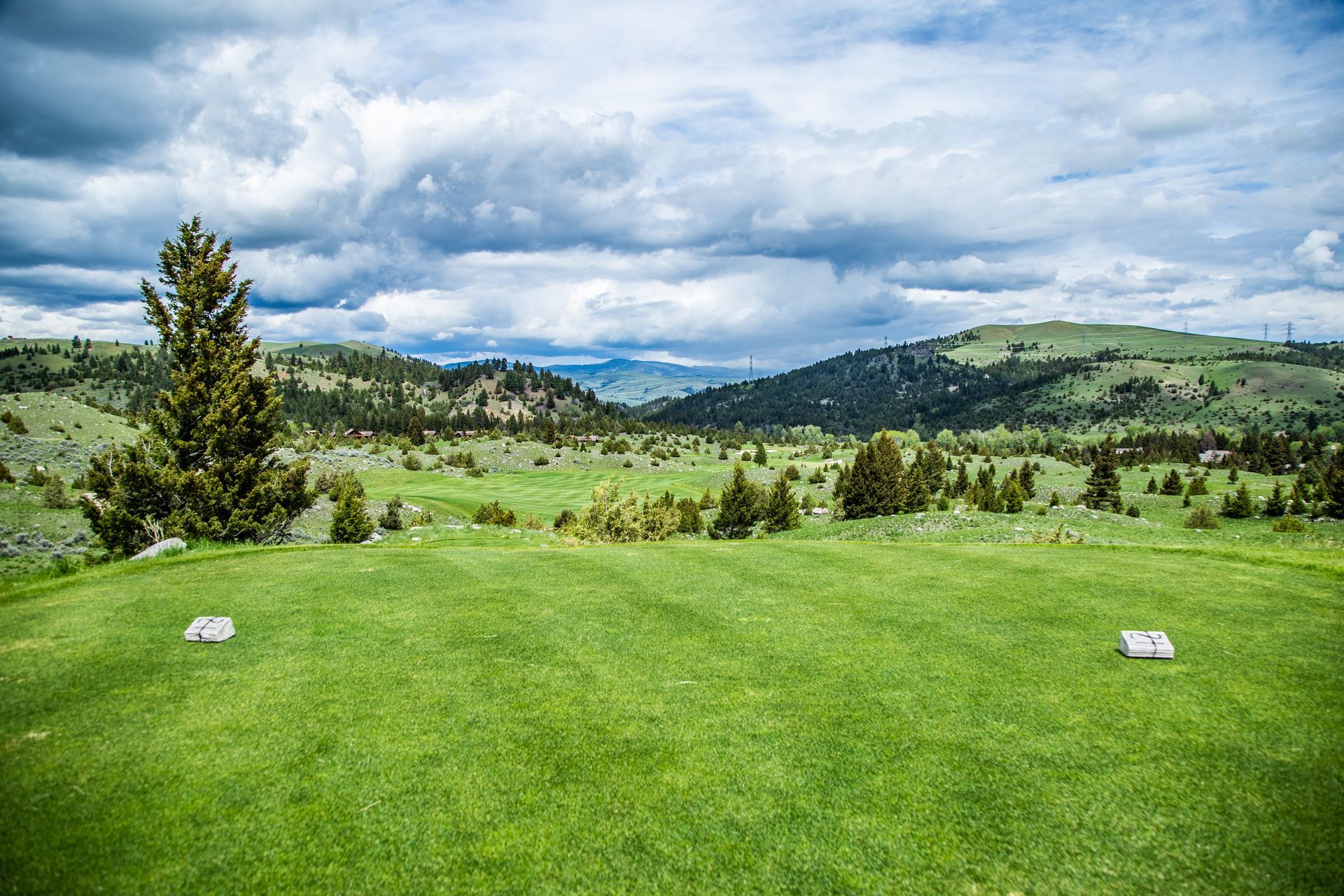 A golf course in the middle of a grassy field with mountains in the background.