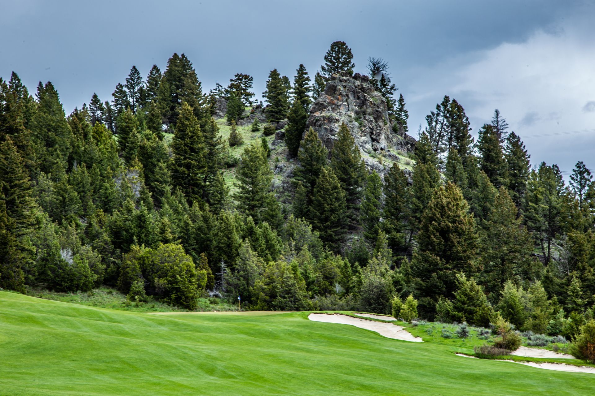 A golf course with a mountain in the background and trees on the side.
