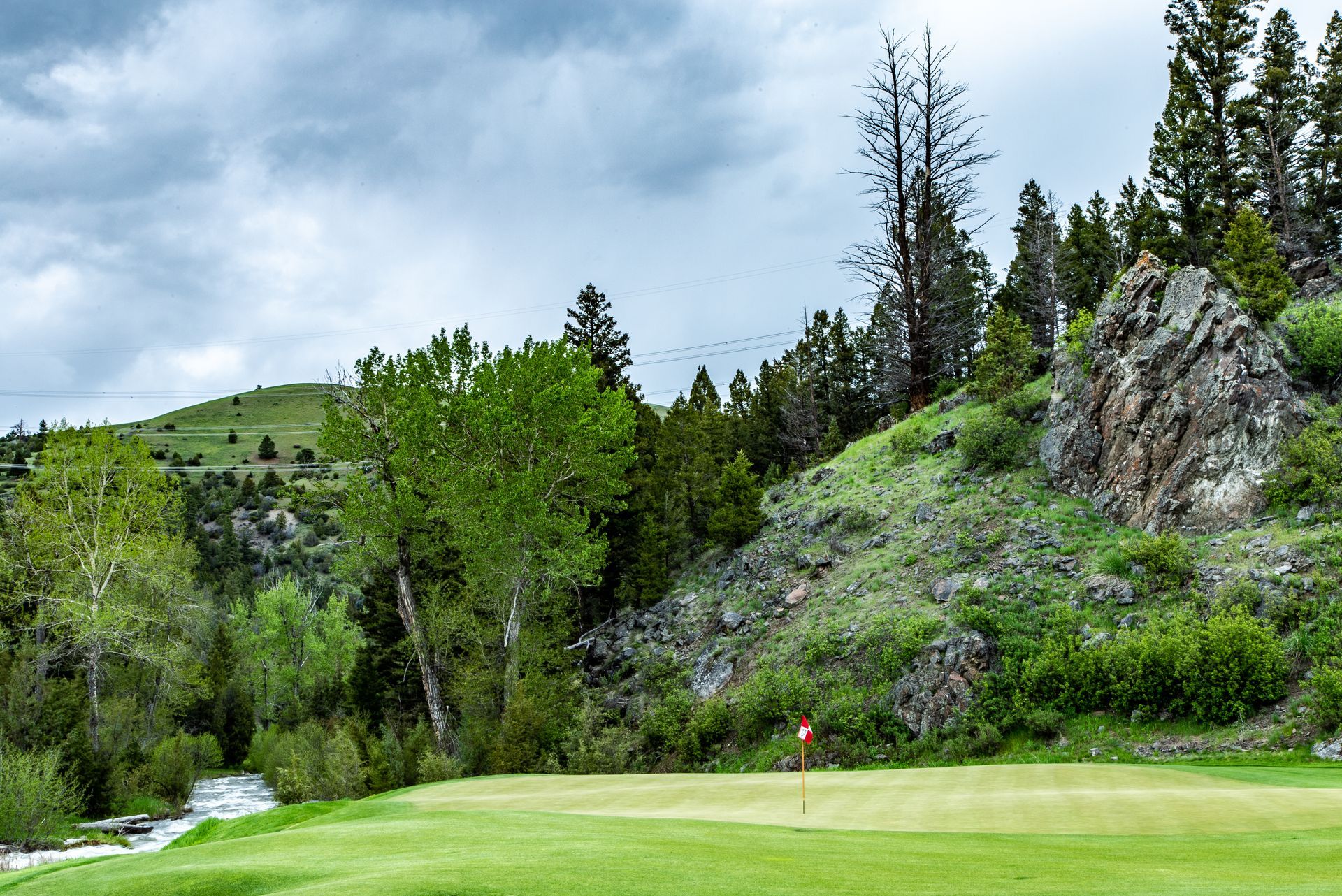 A golf course with a river running through it and trees in the background.