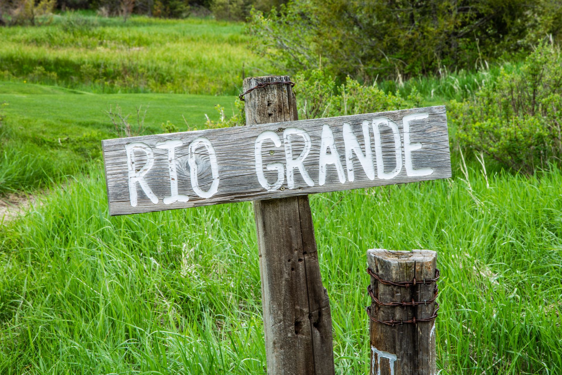 A wooden sign that says rio grande is sitting in the middle of a grassy field.