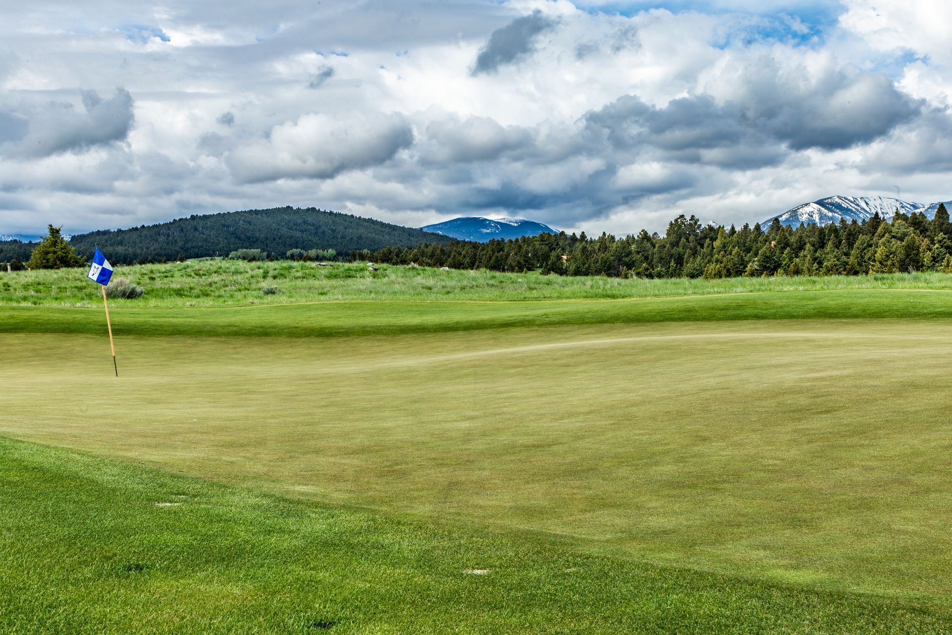 A golf course with mountains in the background and a flag on the green.