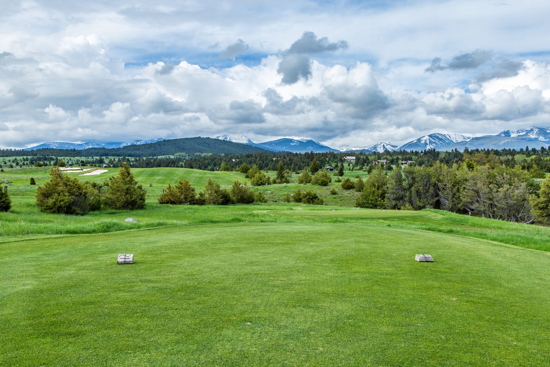 A golf course with mountains in the background and a cloudy sky.