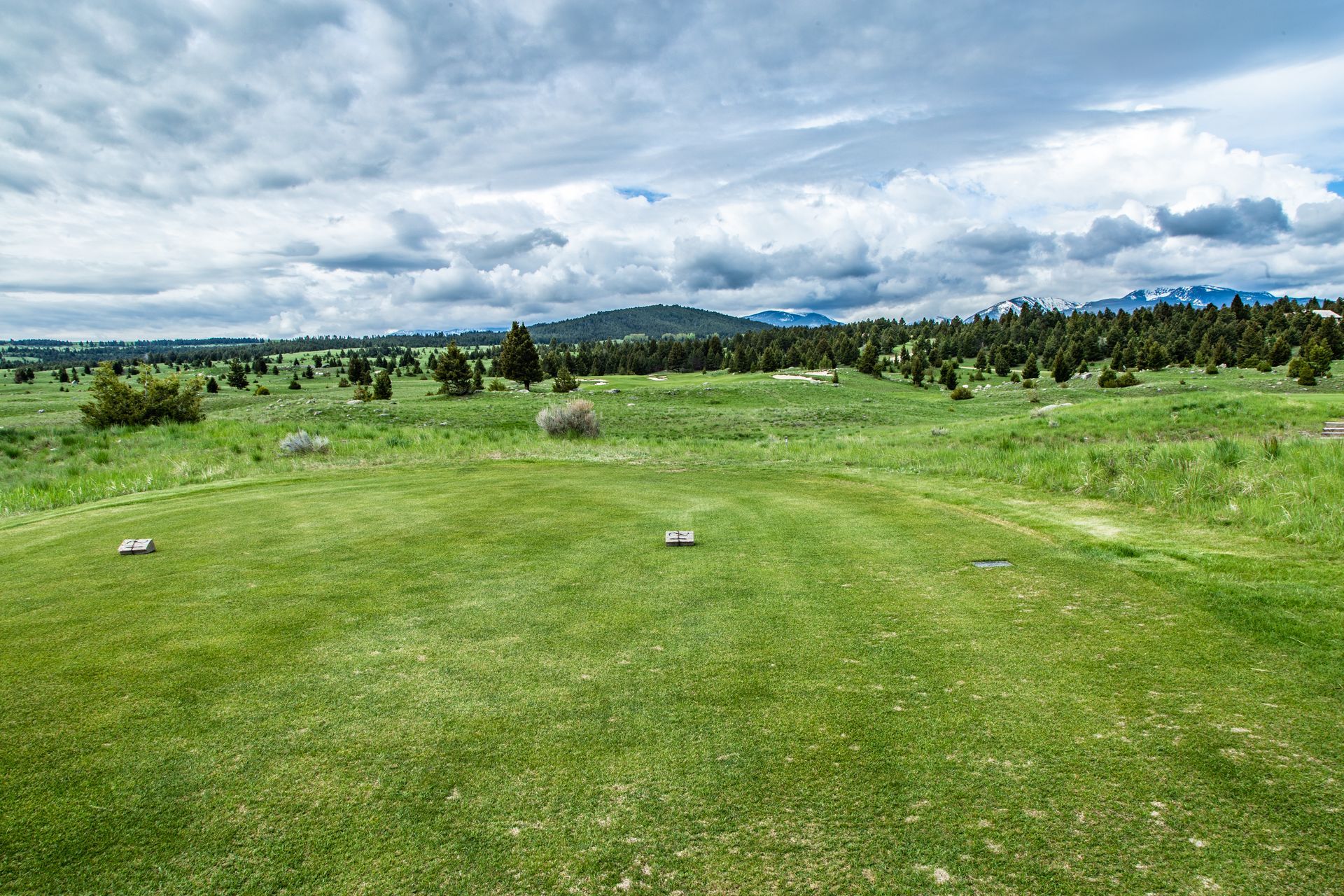 A golf course in the middle of a grassy field with mountains in the background.