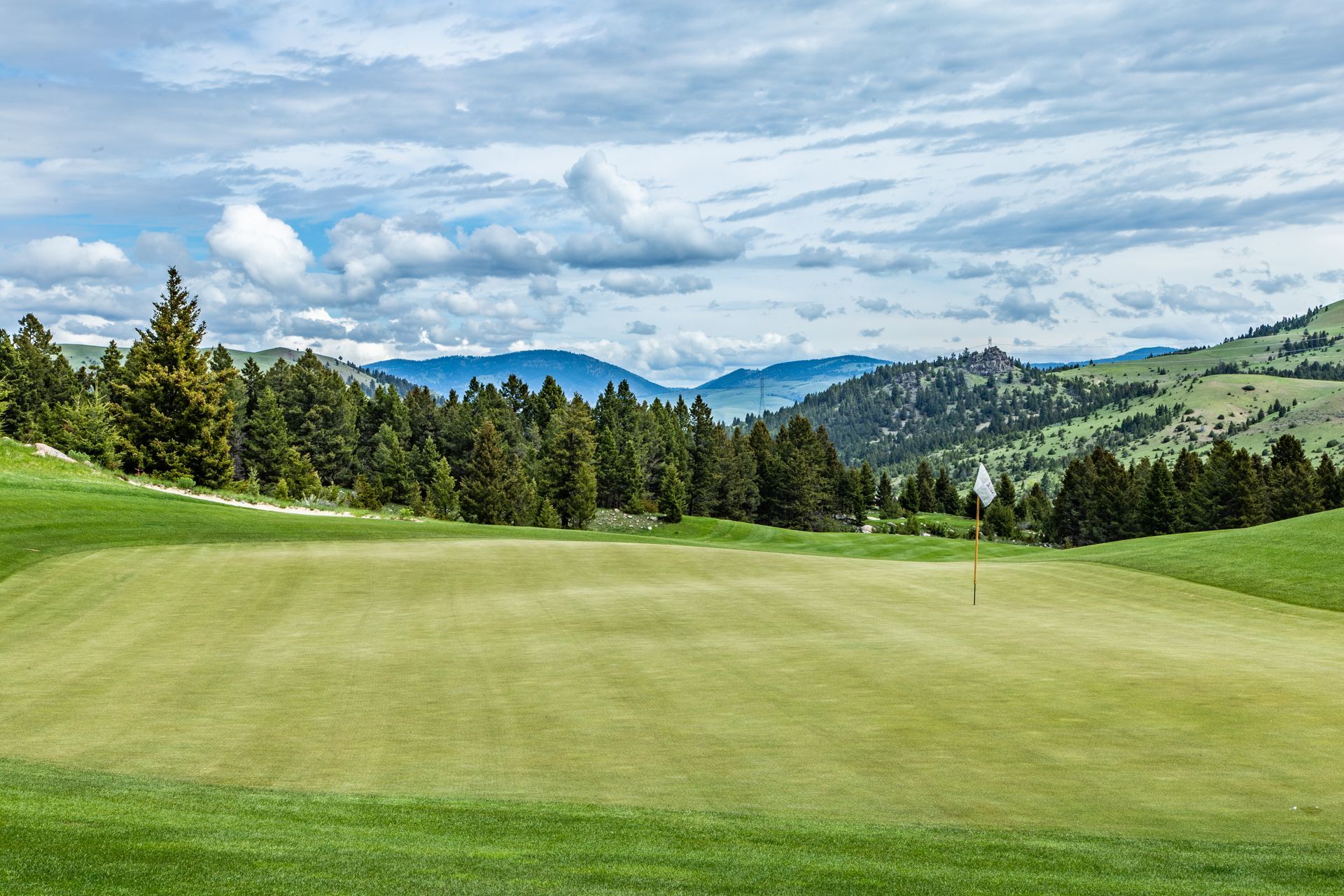 A golf course with mountains in the background and trees in the foreground.