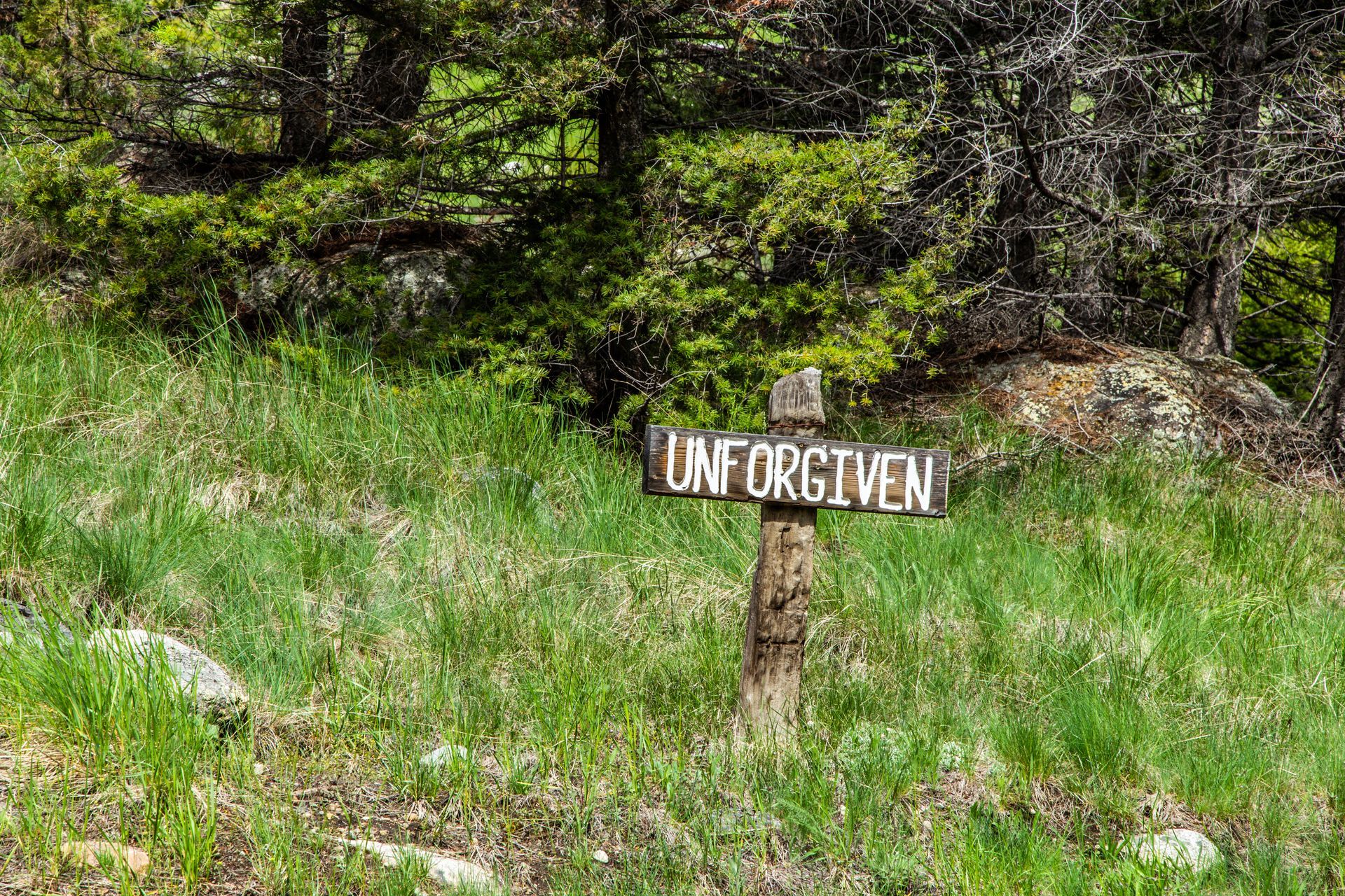 A wooden sign in the middle of a grassy field says `` unforgiven ''.