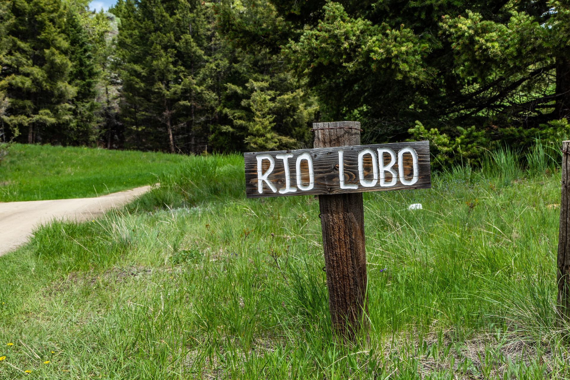 A wooden sign that says rio lobo is in the middle of a grassy field.
