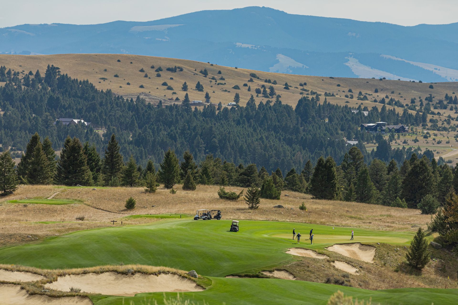 A group of people are playing golf on a golf course with mountains in the background.