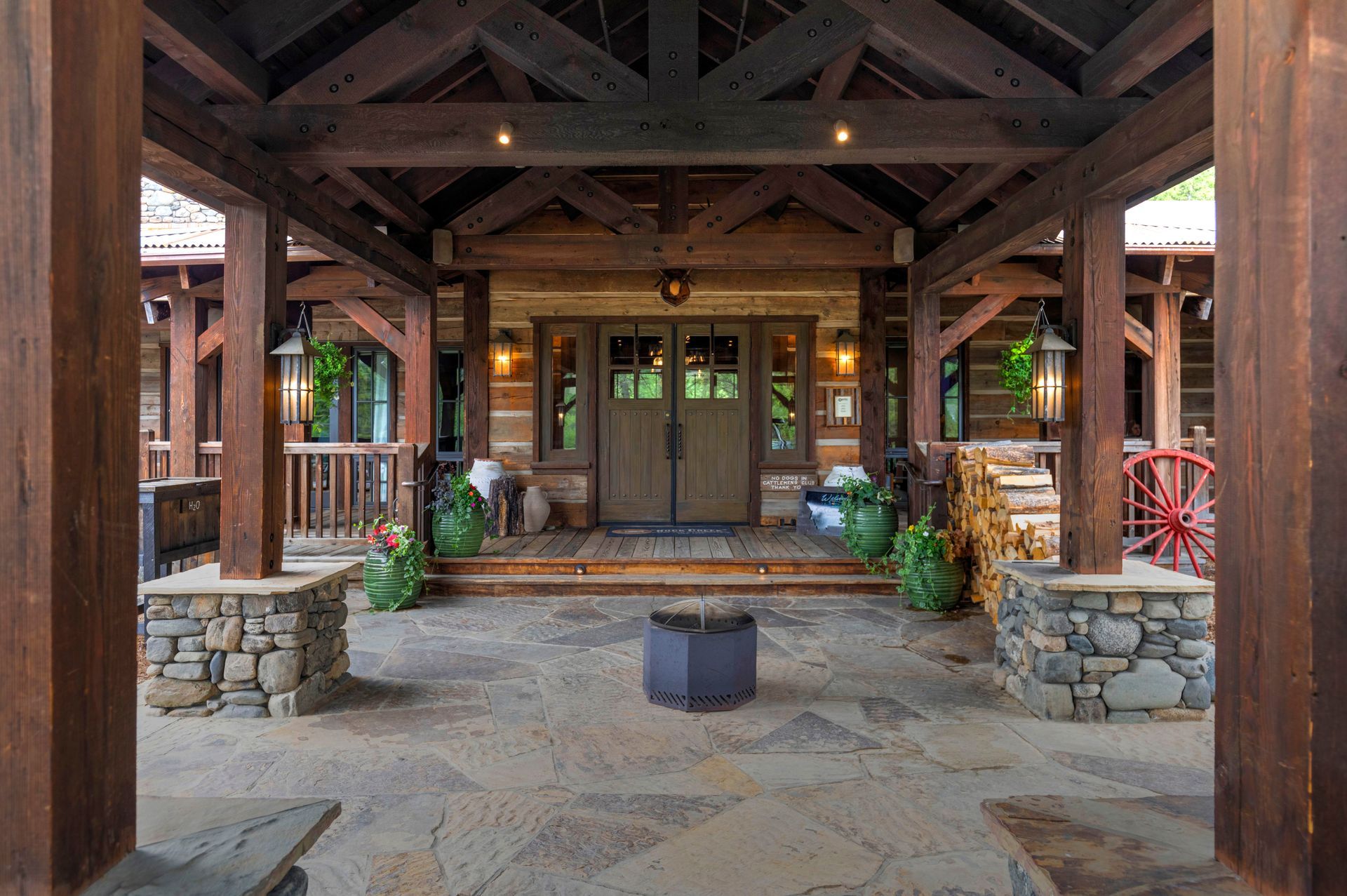 A large wooden house with a stone floor and a fire pit in front of it.
