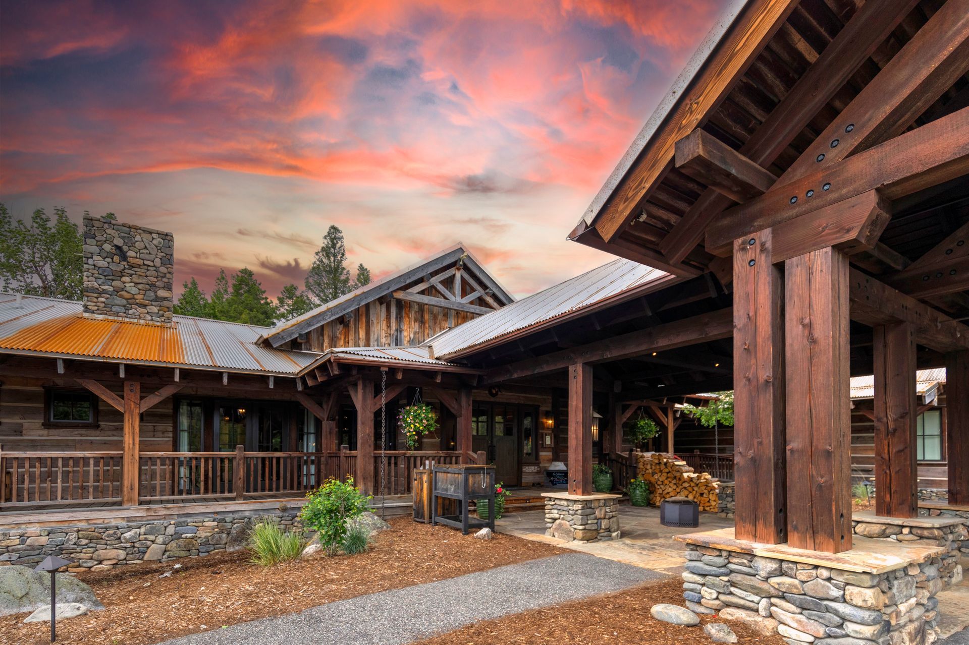 A large log cabin with a covered porch and a sunset in the background.