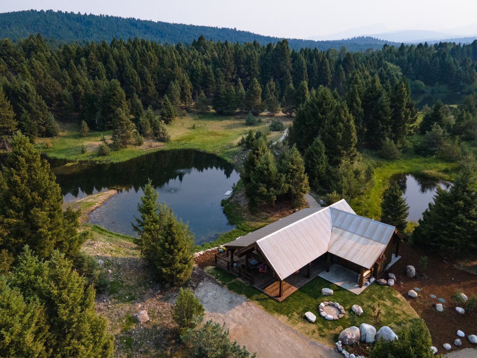 An aerial view of a house with a pond in the middle of a forest.