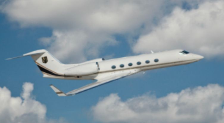 A private jet is flying through a cloudy blue sky.