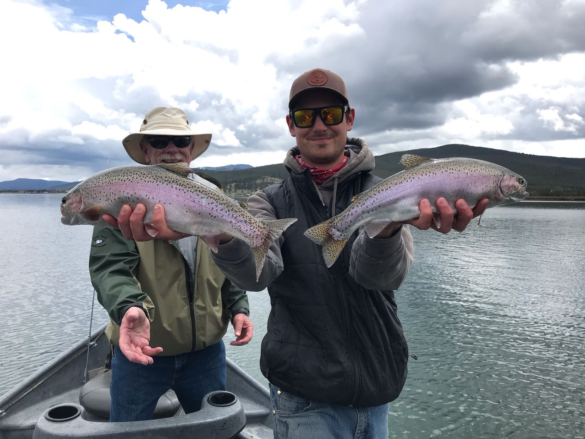 Two men are standing on a boat holding two fish.