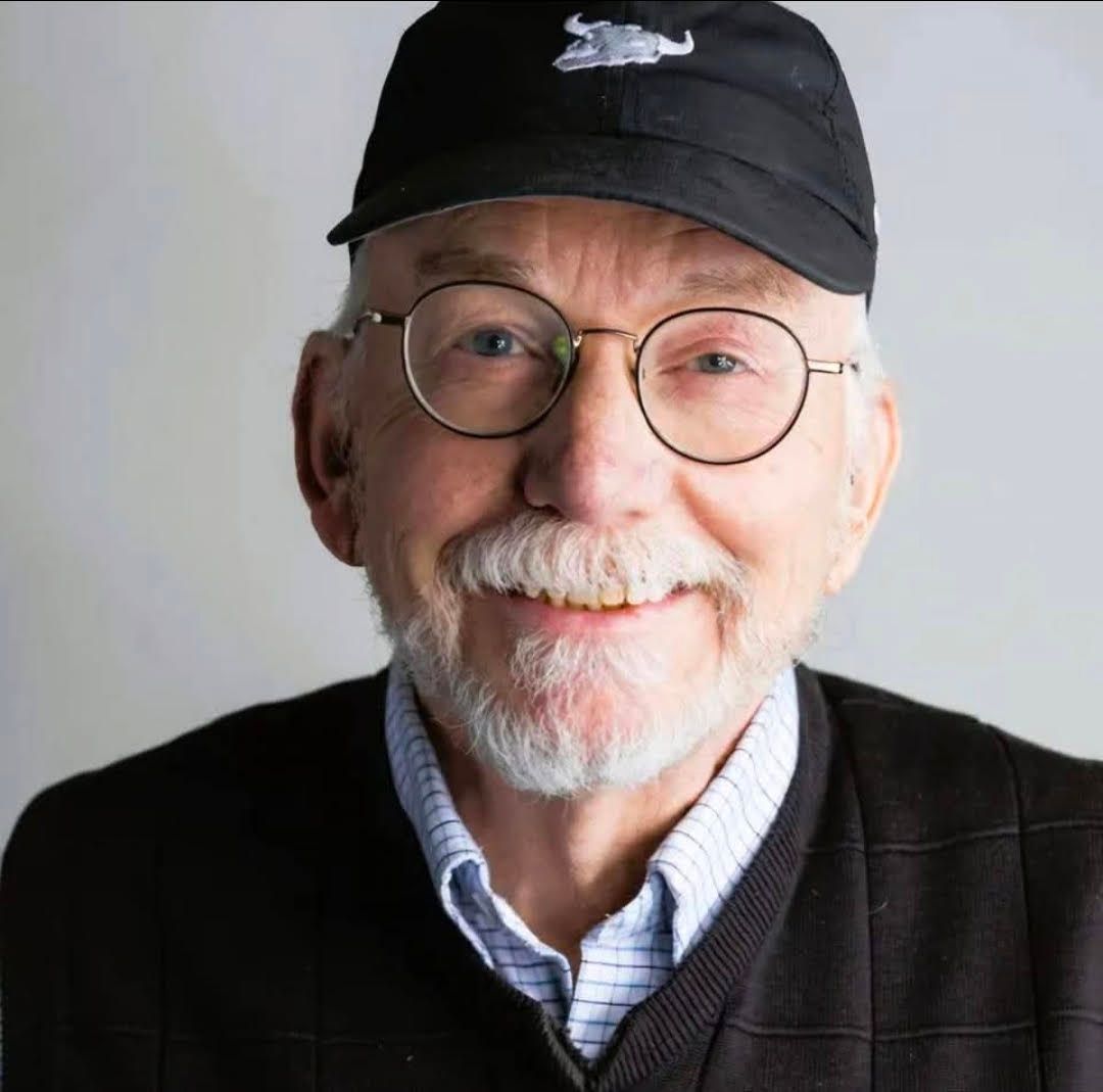 A man wearing a hat and a sweater is standing with his arms crossed.