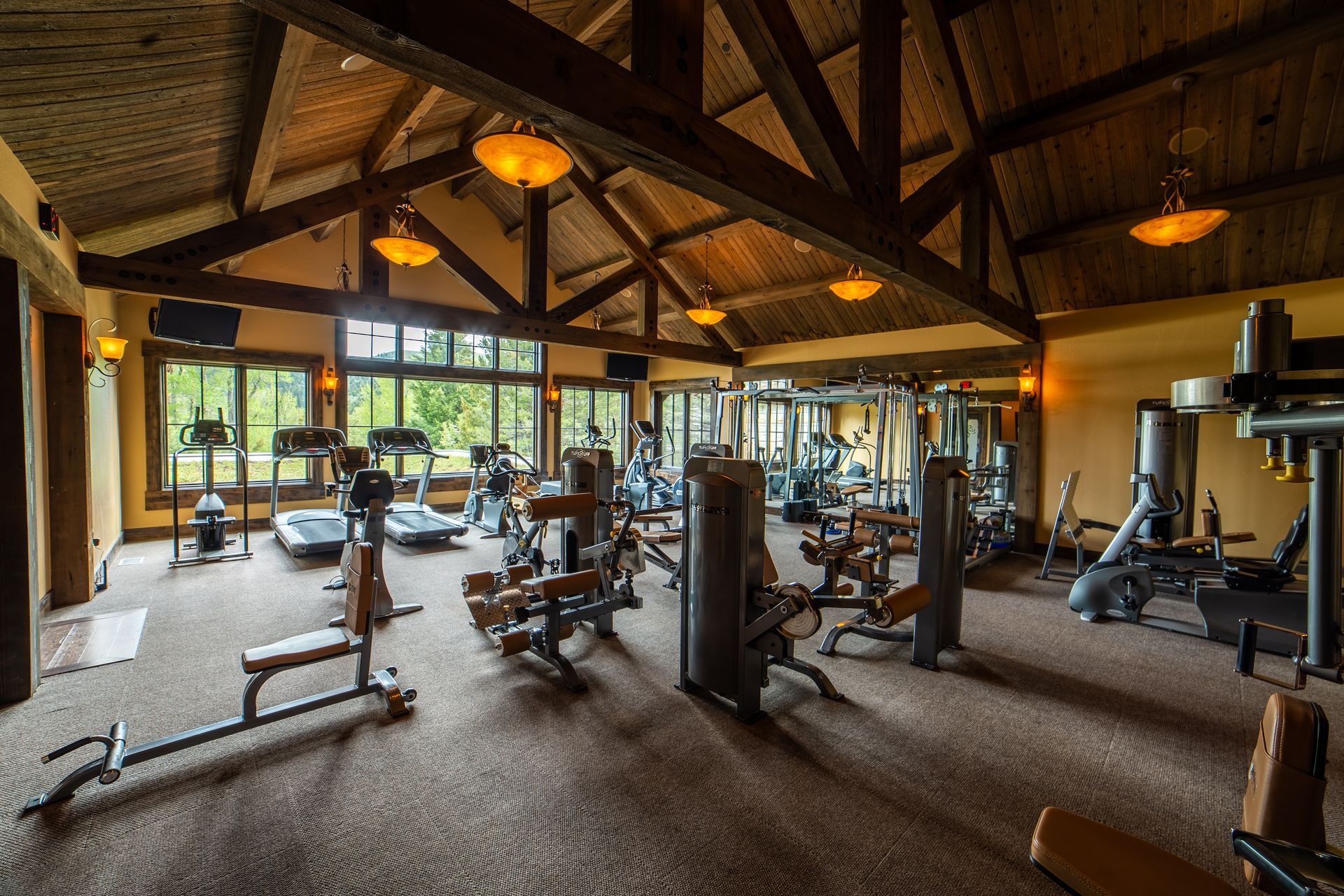 A large gym filled with lots of exercise equipment and a wooden ceiling.