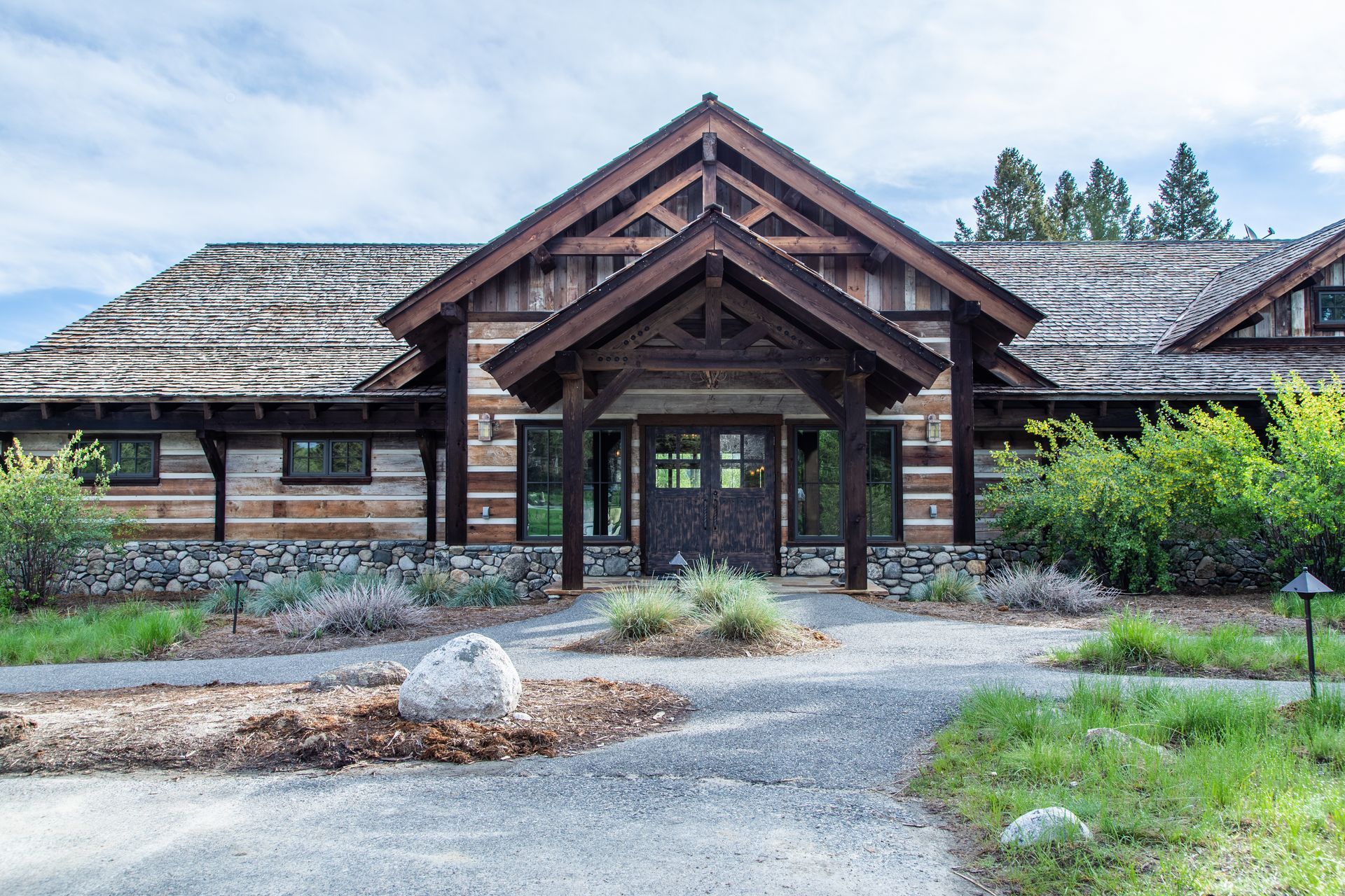 A large log cabin with a thatched roof is surrounded by grass and trees.