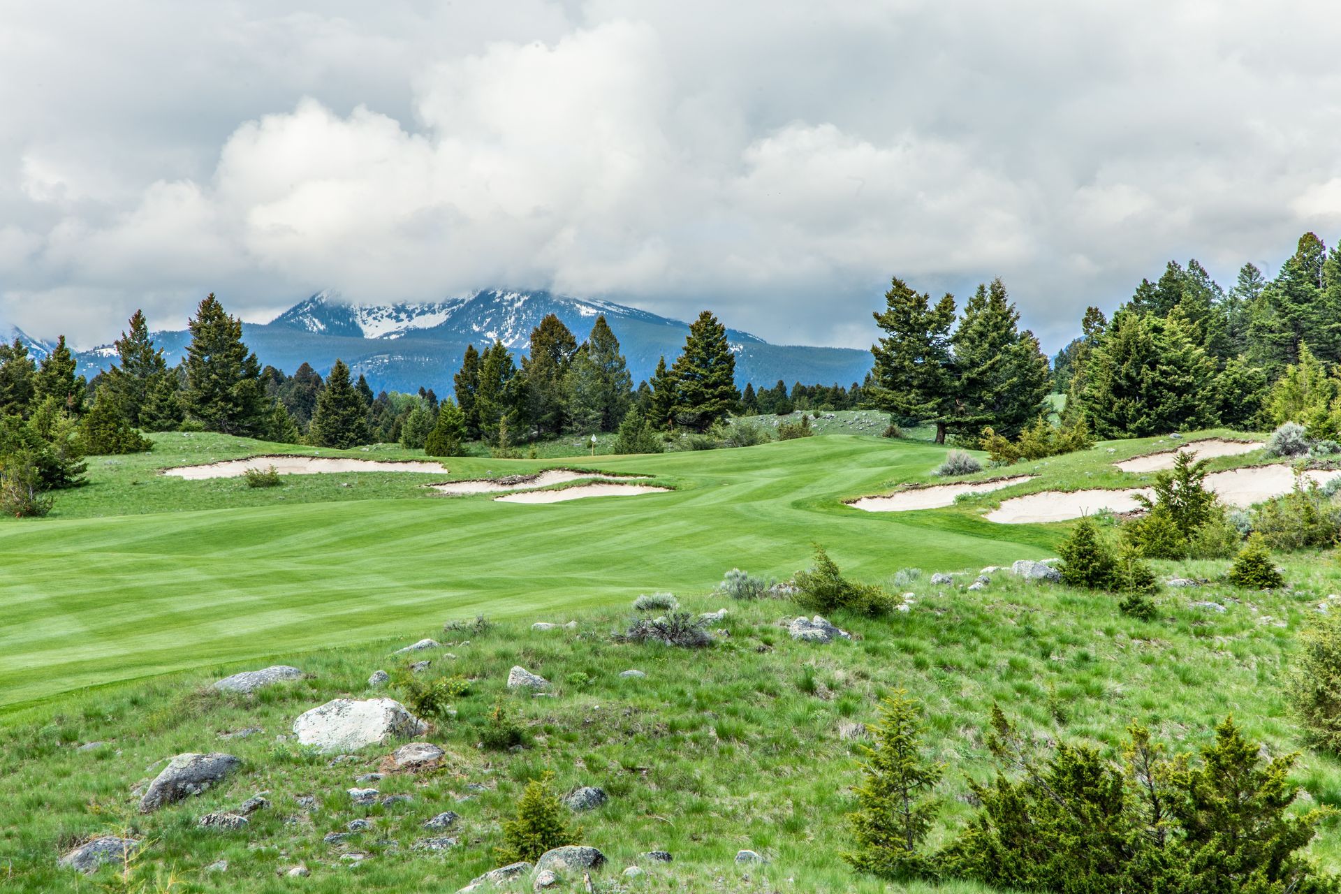 A golf course with mountains in the background and trees in the foreground.