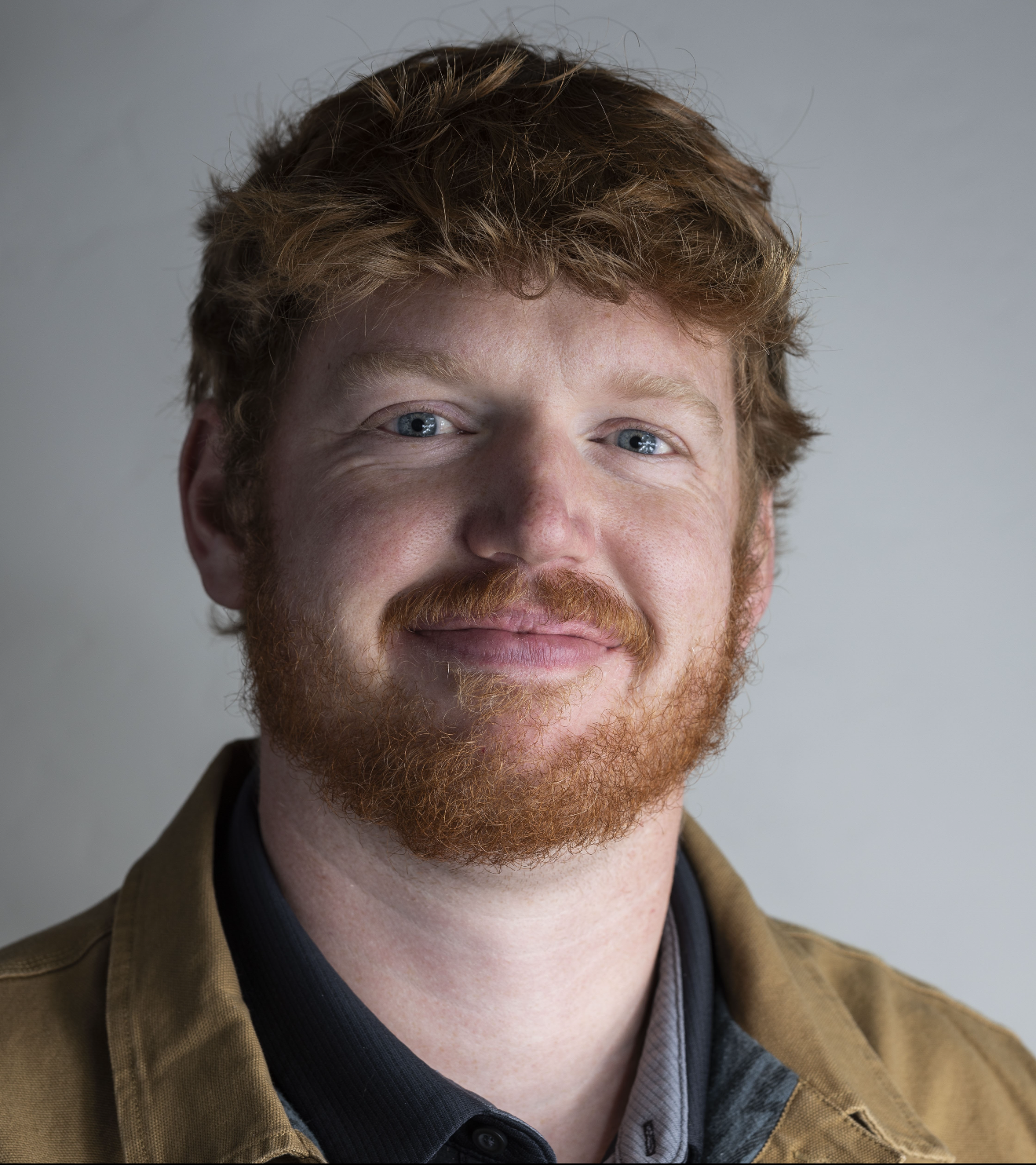 A man with red hair and a beard is wearing a black shirt and smiling.