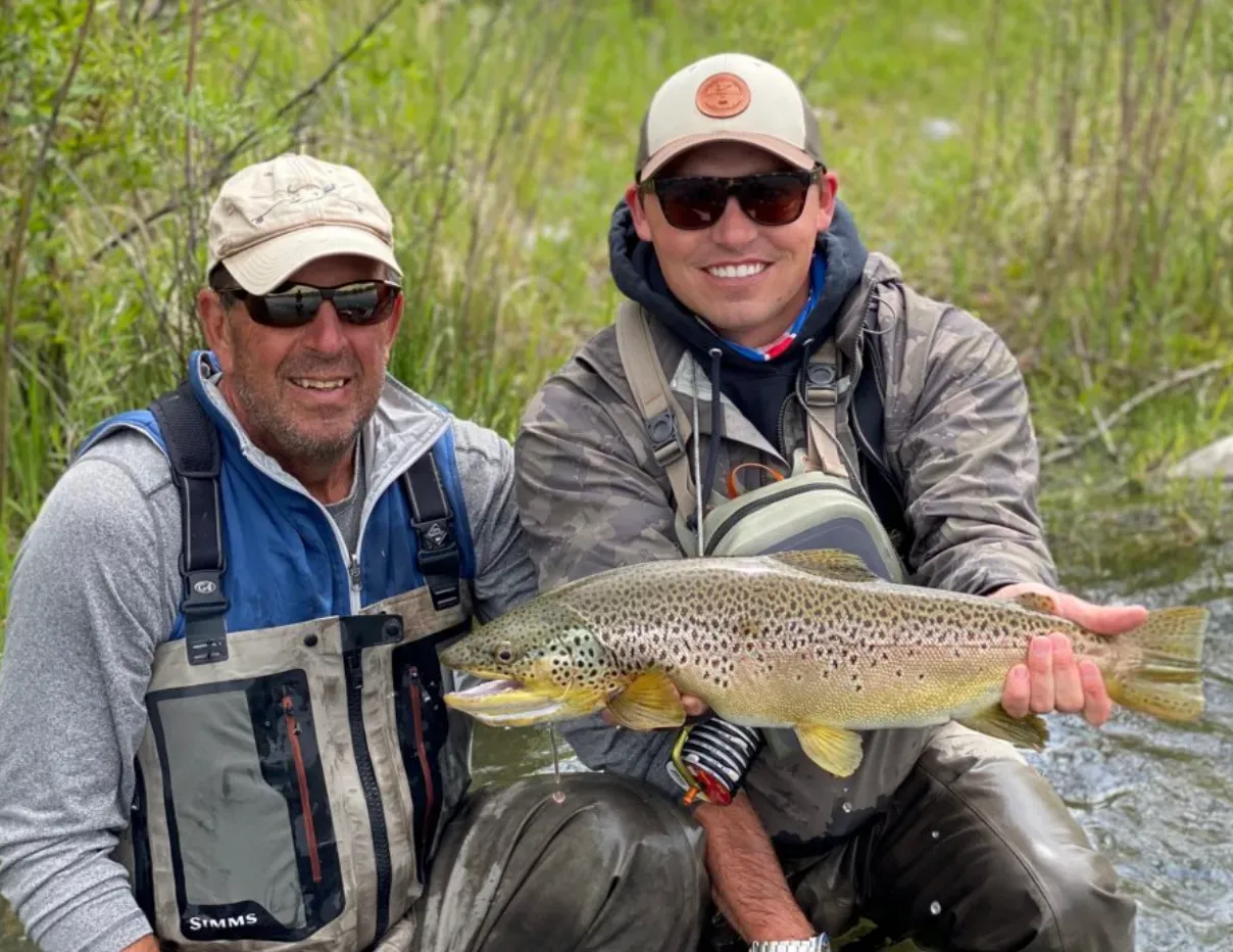Two men are holding a brown trout in their hands.
