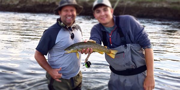 Two men are standing in the water holding a fish.