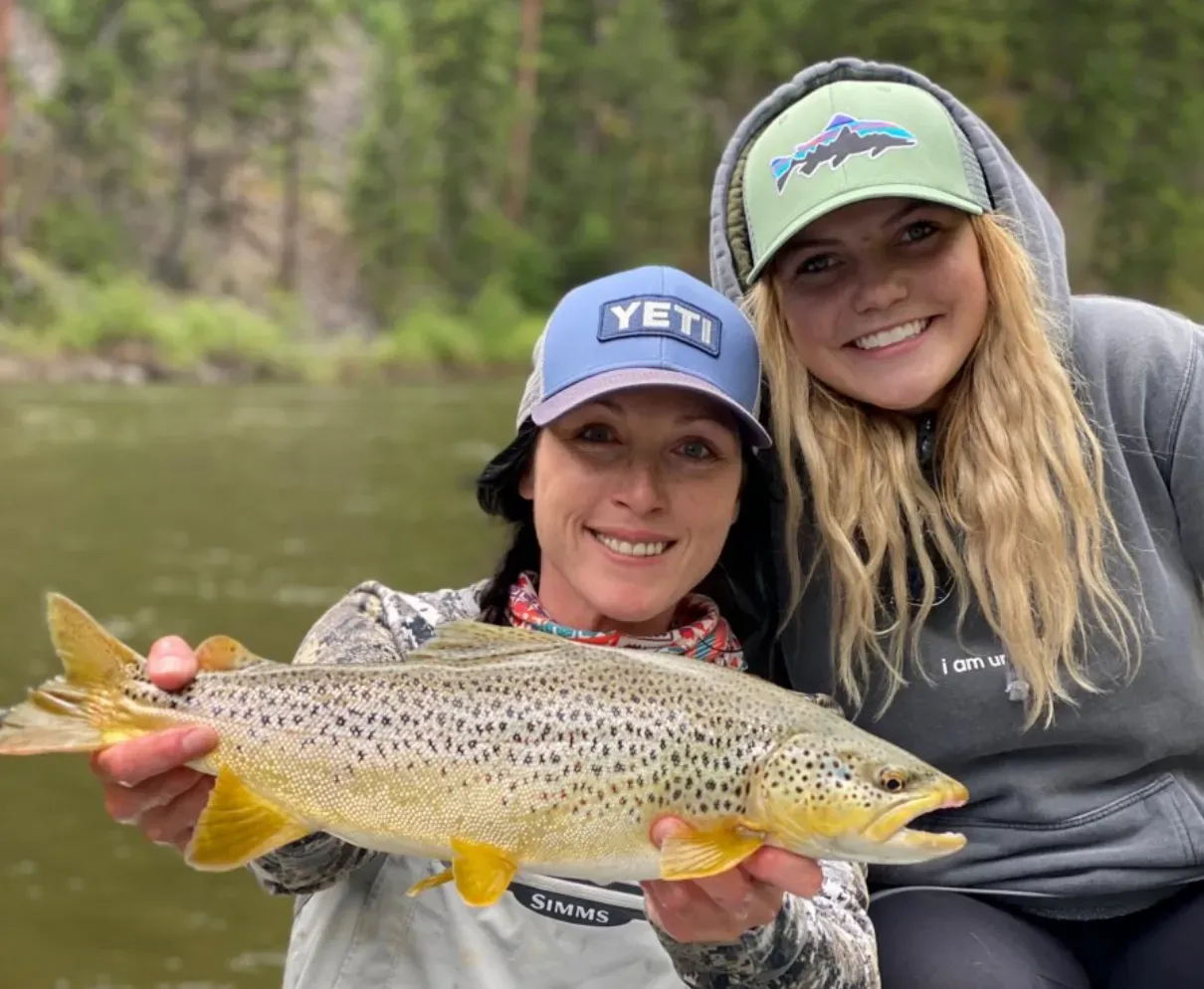 Two women are holding a brown trout in their hands.