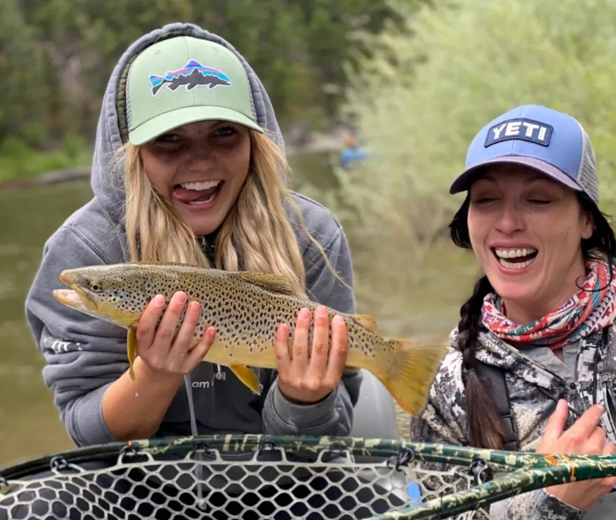 Two women are holding a brown trout in a net.