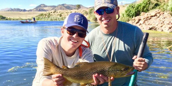 Two men are holding a brown trout in their hands in a lake.