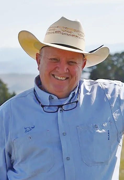 A man wearing a cowboy hat and a blue shirt is smiling.