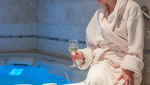 A woman in a bathrobe is sitting in a jacuzzi holding a glass of wine.