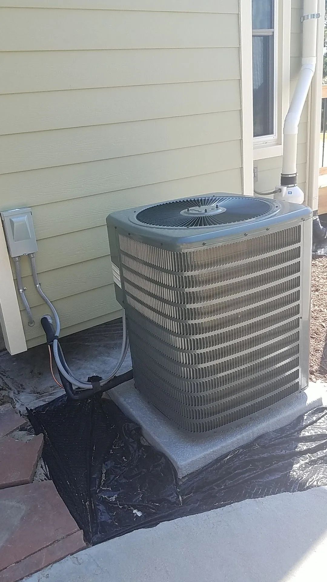 Air conditioning unit outside a building, with a gray box on a concrete base.