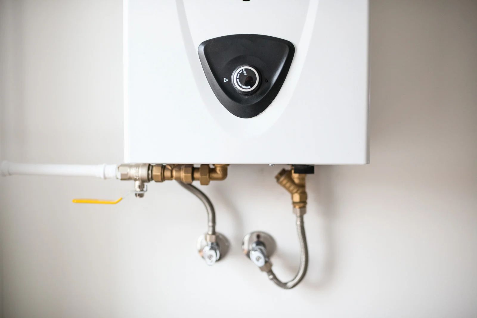 White wall-mounted water heater with brass pipes and valves.