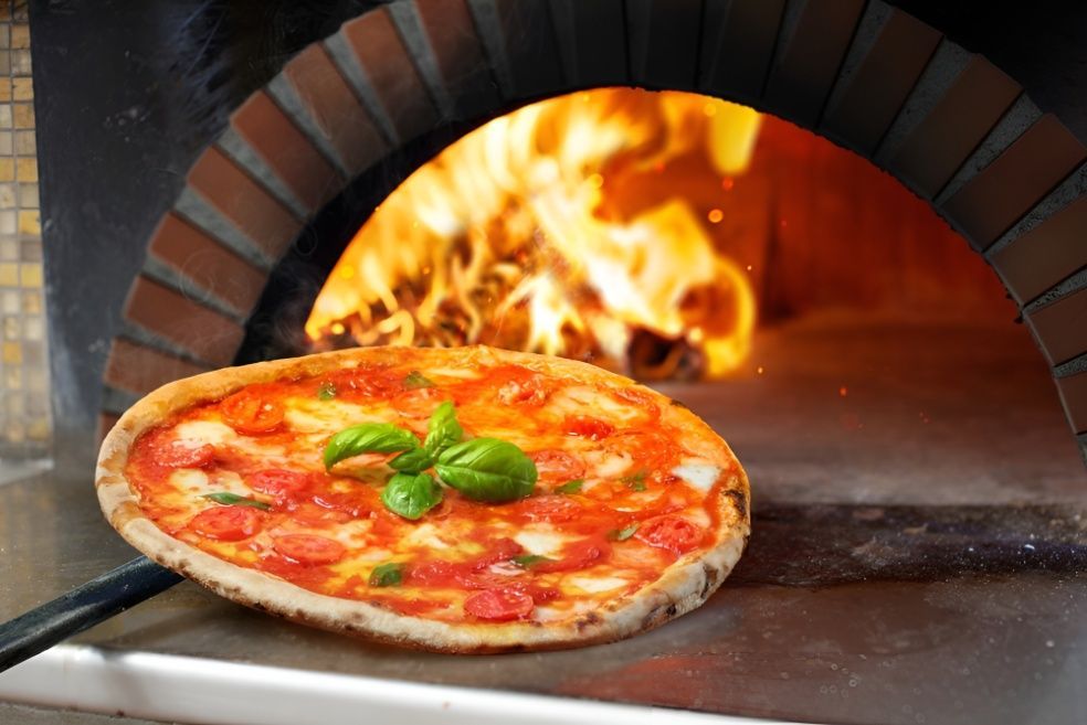 A Pizza is Being Cooked in a Brick Oven Using A Stick — Mulgrave Seafoods In Bungalow, QLD